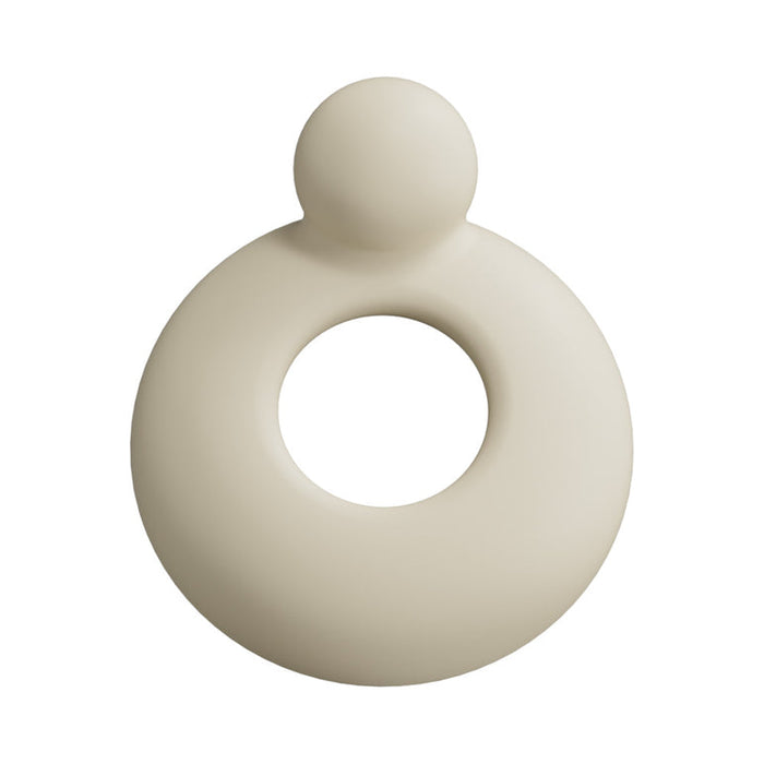 A beige, circular object with a central hole and a small sphere on top—resembling the Spinel App-Controlled, Multi-Attachment Thrusting, Vibrating & Heating Dildo Machine—rests on a white background like an abstract ring or modern ornament.