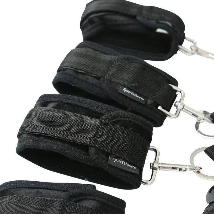 A close-up of the Sportsheets Under the Bed Restraint System showcases black soft restraints with adjustable straps and metal clips. The plush material ensures comfort and secure fastening, making it an ideal bondage bedroom addition. The brand name "Sportsheets" is visible on the straps.