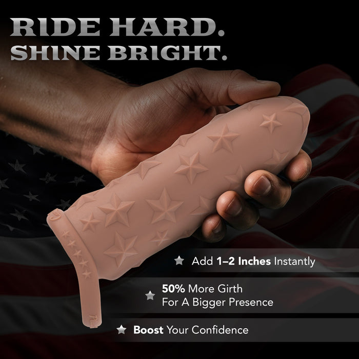 A hand holds the Star Studded Silicone Penis Extender - 6.5 Inch Closed Ended, nude with star patterns and a strap, against a faint American flag. Text: "Ride Hard. Shine Bright." Benefits: added length, more girth, increased confidence.