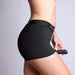 A person wearing the Strap On Me Allure Boxer Style Harness with a dildo attached, shown from the side against a plain light background.