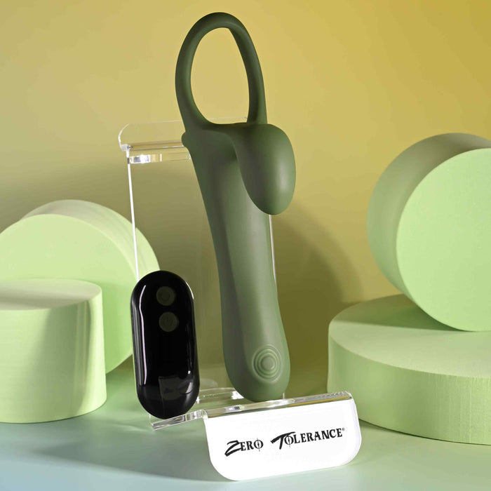 The Strap Tap & Go Girth Enhancer & Tapping Vibrator is shown on clear stands among pastel green cylinders. A white base labeled "Zero Tolerance" and a softly lit yellow-green background highlight this hands-free couples sex toy.