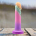 The Sunrise Gaze Textured Silicone Suction Cup 7.5 Inch Dildo—a pastel, column-shaped toy with a rounded swirled top—is upright on a wooden surface outdoors, designed for g-spot stimulation.