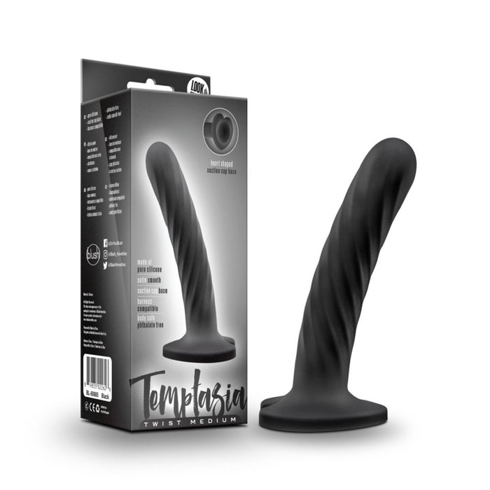 The Temptasia Twist Curved Slim 5 Inch Black Silicone Pegging Dildo, featuring a twisted design and wide base, stands upright by its packaging. This beginner-friendly dildo is strap-on compatible, designed for solo or partnered play.