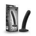 The Temptasia Twist Curved Slim 5 Inch Black Silicone Pegging Dildo, featuring a twisted design and wide base, stands upright by its packaging. This beginner-friendly dildo is strap-on compatible, designed for solo or partnered play.
