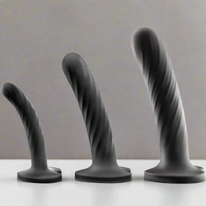 The Temptasia Twist Set of 3 Curved Black Silicone Pegging Dildos features textured, twisted designs for G-spot stimulation in three sizes. Made from body-safe silicone, they stand upright on a white surface against a gray background.