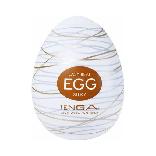 The Tenga Egg Disposable Penis Masturbator - Silky is an egg-shaped white toy with gold swirls and a brown label. Branded "TENGA" with "LIVE WITH WONDER," it’s a perfect disposable travel masturbation sleeve.