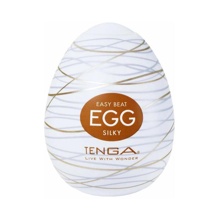 The Tenga Egg Disposable Penis Masturbator - Silky is an egg-shaped white toy with gold swirls and a brown label. Branded "TENGA" with "LIVE WITH WONDER," it’s a perfect disposable travel masturbation sleeve.