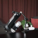 The Handy Handsfree Desk Mount holds a black water bottle and a small clear container with its adjustable articulating arm. In the softly blurred background, you can see a dark curtain, plant, and tech devices.