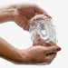Two hands hold and gently squeeze The Handy TrueGrip Gen 2 Sleeve—a longer, thicker, stretchy, clear stroker sleeve with textured bumps—against a plain white background.