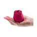 A hand with pink-painted nails holds The Rose Powerful Clitoral Suction Air Pulsation Vibrator, a soft, flower bud-shaped stimulator in delicate pink.