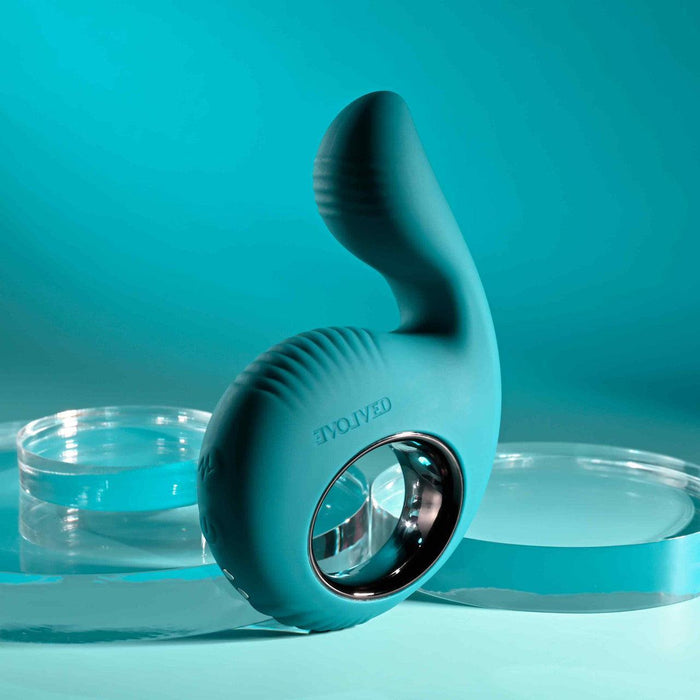 Teal silicone shallow penetration vibrator with a thumb-shaped branch, textured finger loop, and metallic trim.
