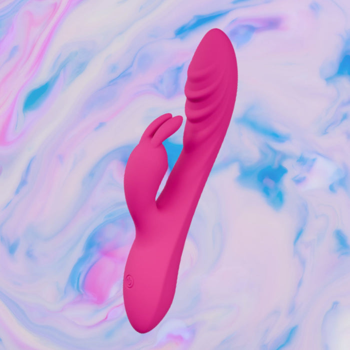 The Wild Lust Slim Beginner G-Spot Rabbit Vibrator, a pink silicone toy with a curved shaft and rabbit-shaped clitoral stimulator, is displayed against a pastel marbled blue, pink, and white background.