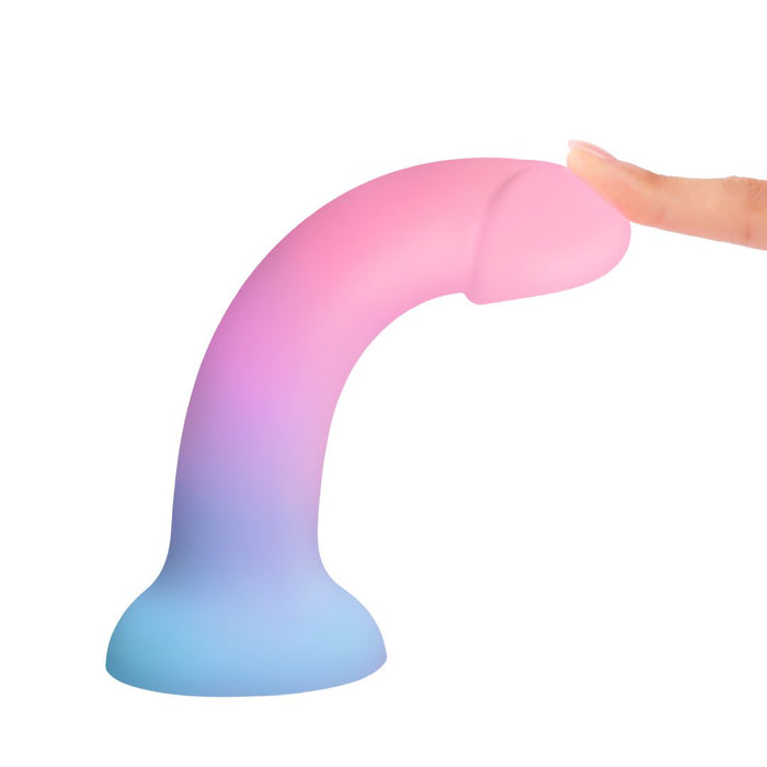 A person's finger gently touches the Utopia Sleek 7 Inch Pink and Blue Ombre Silicone Dildo with Suction Cup, featuring a blue-to-pink gradient design, against a white background.