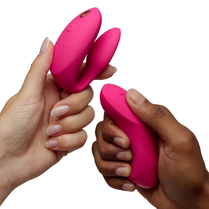 Two hands hold the We-Vibe Chorus Pro Wearable Couples' Vibrator with Triple Motors & Remote against a white background—one highlighting its couple’s use, the other showing off its curved, G-spot-stimulating design.
