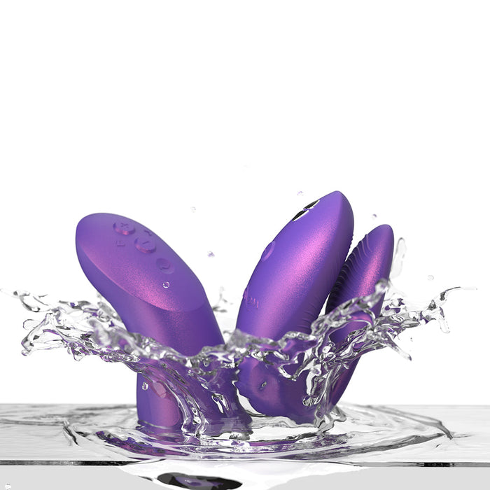 Three We-Vibe Chorus Pro Wearable Couples’ Vibrators with triple motors and remote, featuring Fusion Wave Technology, splash into clear water, creating droplets and ripples on a white background.
