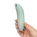 A hand holds the We-Vibe Melt 2, a mint green, curved silicone stimulator with a rounded tip and opening for pleasure air clitoral stimulation, against a white background.
