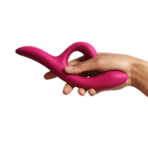 A hand holds the We-Vibe Nova 2 Powerful Flexible G-Spot Rabbit Vibrator—pink, curved silicone with an ergonomic looped handle—against a plain white background.