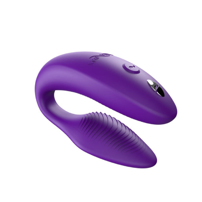 A sleek, C-shaped personal massager, the We-Vibe Sync Remote and App Controlled Wearable Couples Vibrator in purple by We-Vibe features an upper segment with a control button and small indicator light. The lower segment is designed with a textured surface for enhanced stimulation, constructed from smooth and durable materials.