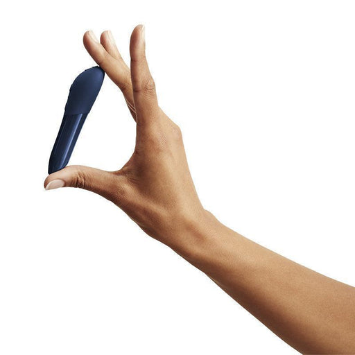 A hand holds the We-Vibe Tango X Powerful Waterproof Bullet Vibrator—small, curved, and dark blue—between the thumb and index finger against a plain white background.