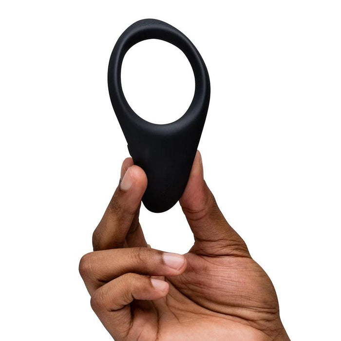 Hand holding a black, flexible silicone We-Vibe Verge 2 vibrating cock ring with a teardrop-shaped stimulator.