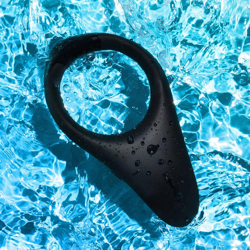 Black silicone We-Vibe Verge 2 vibrating cock ring resting in rippling blue water with droplets on its surface.