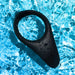 Black silicone We-Vibe Verge 2 vibrating cock ring resting in rippling blue water with droplets on its surface.