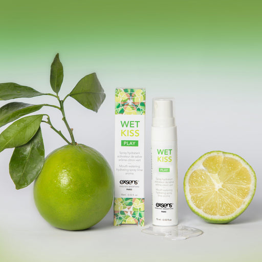 A bottle and box of Wet Kiss Lime Moisturizing Saliva Spray are shown beside whole and halved limes with leaves, evoking a fresh lime scent on a white surface against a green gradient background.