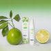 A bottle and box of Wet Kiss Lime Moisturizing Saliva Spray are shown beside whole and halved limes with leaves, evoking a fresh lime scent on a white surface against a green gradient background.