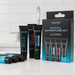 Four black tubes from the Wicked Anal Adventure Variety Pack—containing 4 travel-sized anal lubricants—stand by their box on a white countertop, with extra lubricant tubes in front and a white tiled wall as the backdrop.