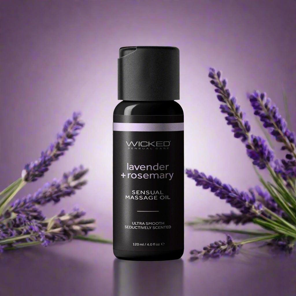 A bottle of Wicked Sensual Care lavender and rosemary massage oil is displayed upright against a purple gradient background, surrounded by sprigs of fresh lavender flowers.