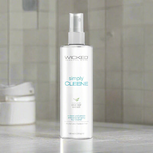 A clear 4 oz spray bottle labeled "Wicked Simply Cleene Antibacterial Toy Cleaner" sits on a bathroom counter. Alcohol-free and made with natural olive leaf extract, it offers a gentle yet effective clean for toys.