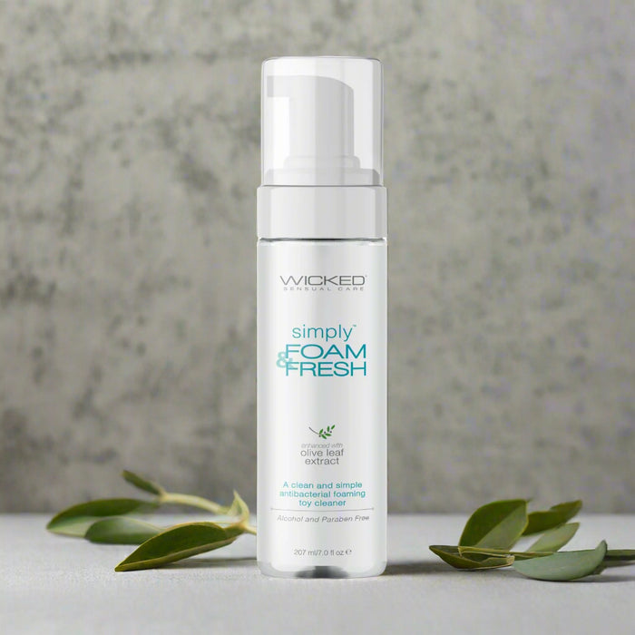 A 207 ml (6 fl oz) white bottle of Wicked Simply Foam And Fresh Toy Cleaner features a pump dispenser, contains olive leaf extract and essential oils, and is labeled alcohol and paraben-free.