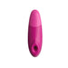 The Womanizer Enhance Pleasure Air + Vibration Clit Stimulator is a pink, oval massager with a rounded top and circular opening, offering rumbly vibrations. Photographed on a white background.