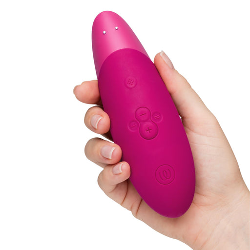 Hand holding a pink, silicone Womanizer Enhance clit stimulator with intuitive control buttons and air technology.