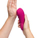A person holds the Womanizer Enhance Pleasure Air + Vibration Clit Stimulator, its rounded tip aimed at their palm, highlighting its powerful rumbly vibrations against a white background.