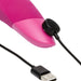 A close-up of the Womanizer Enhance Pleasure Air + Vibration Clit Stimulator being charged with a visible magnetic USB cable, highlighting its pink design and rumbly vibrations.