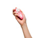 A hand holds the Womanizer Liberty 2 Pleasure Air Travel Sized Clitoral Stimulator, a small pink, oval device with white buttons and a circular white tip for clitoral pleasure air technology, shown against a plain white background.