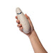A hand holds a pale beige, oval Womanizer Premium 2 Pleasure Air Clitoral Stimulator with three buttons and a blue accent against a white background.