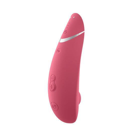 The Womanizer Premium 2 Pleasure Air Clitoral Stimulator, a pink device with a curved shape, multiple buttons, and a silver accent near the top, is photographed on a white background.