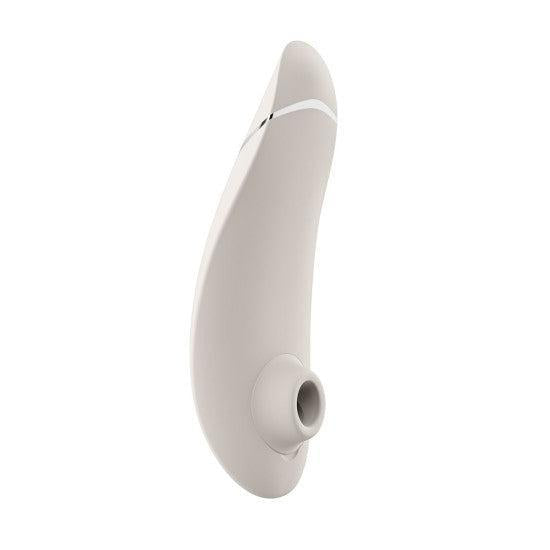 The Womanizer Premium 2 Pleasure Air Clitoral Stimulator is a beige, curved, handheld device with a rounded tip and small circular opening, designed for intimate use and shown against a white background.
