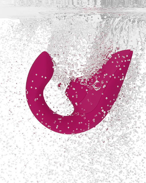A magenta, U-shaped object submerged in water, surrounded by numerous bubbles, creating a dynamic and vibrant scene. The Womanizer Blend Pleasure Air Clitoral & G-Spot Rabbit - Pink, resembling a rabbit vibrator with dual stimulation features, is set against a white background, highlighting its color and design.