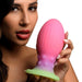 A woman with long dark hair and red lipstick holds the Xeno Egg Glow In The Dark Extra Large Thick Silicone Egg, posing in front of a white background.