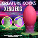 A promo image for the "Xeno Egg Glow In The Dark Extra Large Thick Silicone Egg," featuring its pink and green beaded texture, strong suction base, and glowing effect on a vibrant space-themed background with features highlighted.