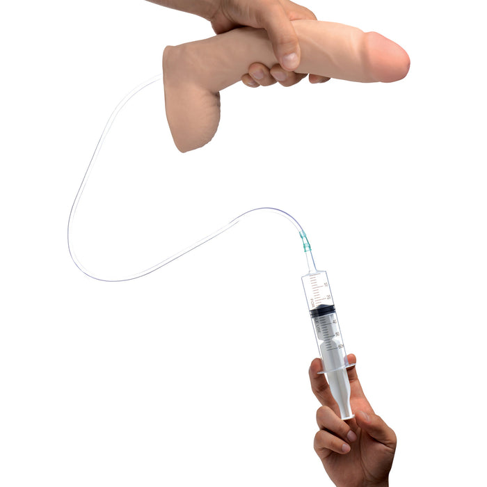 The Loadz Squirting 10 Inch Massive Dildo - Vanilla is shown in one hand, with tubing attached to a syringe held by another hand, all set against a plain white background.