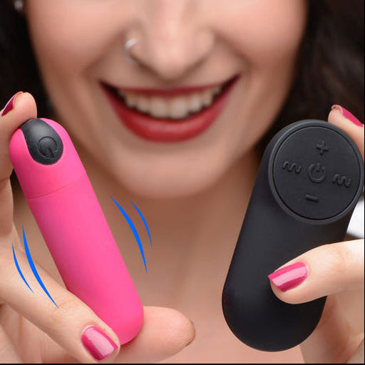 A smiling woman with pink nails and red lipstick holds the BANG! Vibrating Bullet with Remote Control, both featuring power buttons; blue lines illustrate vibration.