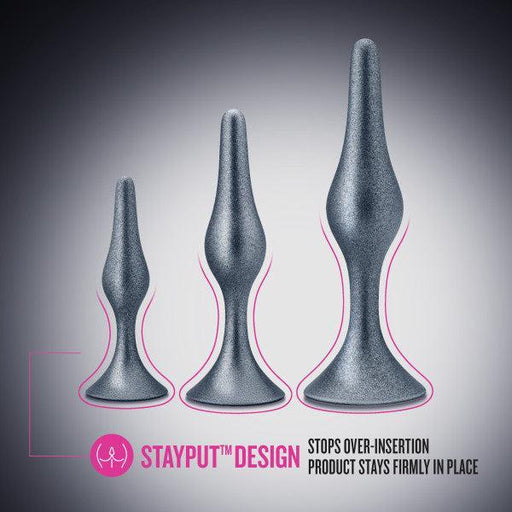 Three grey butt plugs of varying sizes from the Anal Adventures First Time Kit by Blush are presented vertically, with the smallest on the left and the largest on the right. A highlighted caption reads, "STAYPUT™ DESIGN" with text underneath stating, "Stops over-insertion; product stays firmly in place." Discover the innovative Anal Adventures First Time Kit.