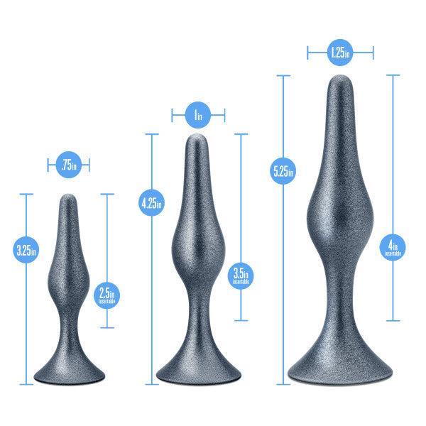 Three gray, metallic-looking, cone-shaped objects of varying sizes and rounded bases. From left to right, they measure 3.25 inches, 4.25 inches, and 5.25 inches in height. Blue arrows indicate the width and height of each object—part of the Blush Anal Adventures First Time Kit with 3 Flexible Butt Plugs featuring StayPut technology.
