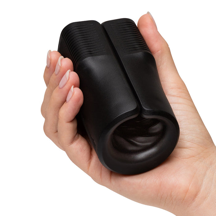 A hand holds a black, cylindrical device with a textured surface and open end, resembling the Arcwave Zing Adjustable Vibrating Silicone Masturbator designed for men's pleasure.