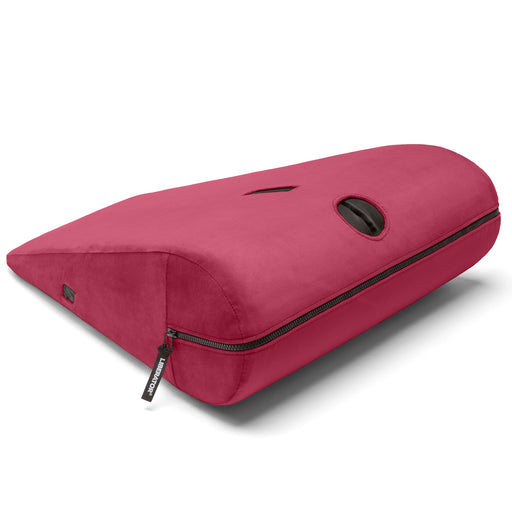 The Liberator Axis Magic Wand Hands-Free Sex Toy Mount, a red wedge-shaped ergonomic pillow with a black circular handle and zippered compartment, is shown on a white background and doubles as a hands-free wand holder.