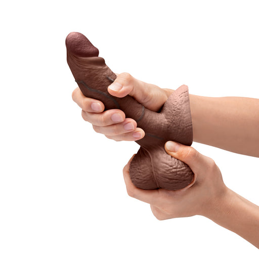 A person holding the b-Vibe Slipskin Realistic 6 Inch Girthy Silicone Dildo in Chocolate Tone, which is crafted for a lifelike appearance.